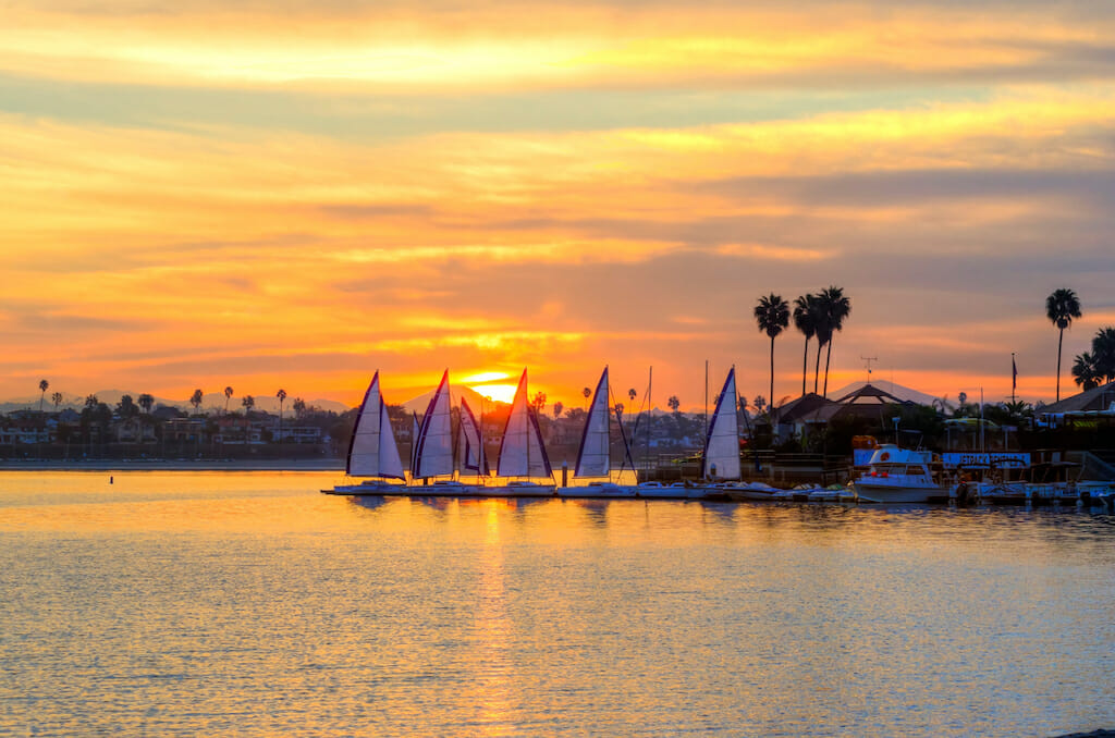 The sunrise over Sail bay in Mission Bay over the Pacific beach in San Diego, California in the United States of America. A view of the palm trees, sail boats and beautiful saltwater bay at sunset.