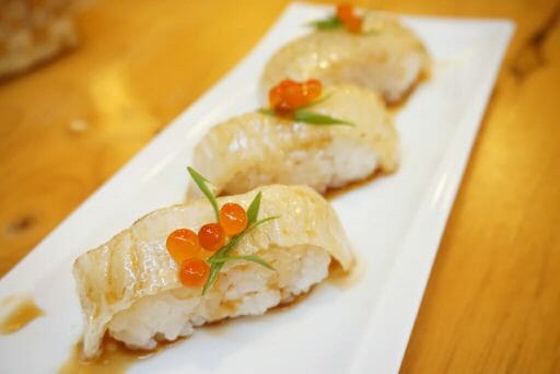 Aburi engawa sushi - Grilled flatfish (Fluke fin) on rice topping with salmon roe (Ikura) served with wasabi and pickled ginger, Japanese traditional food.