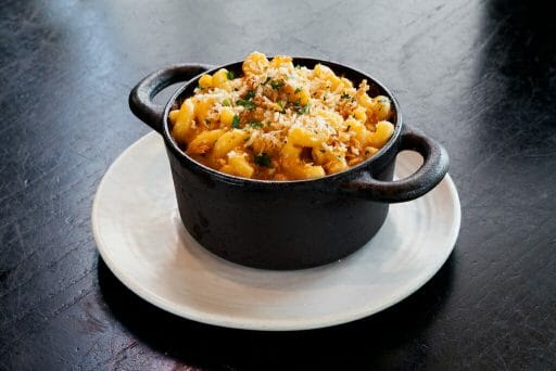 Gourmet mac and cheese with breadcrumbs served in a black pot on a dark table.