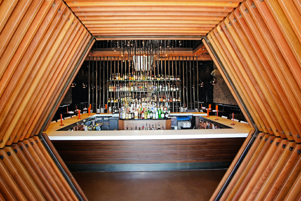 A hexagonal entrance opens up to an illuminated bar with white countertops and a dazzling chandelier