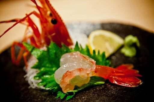 Shrimp head with sashimed shrimp and shinso leaves on a black plate