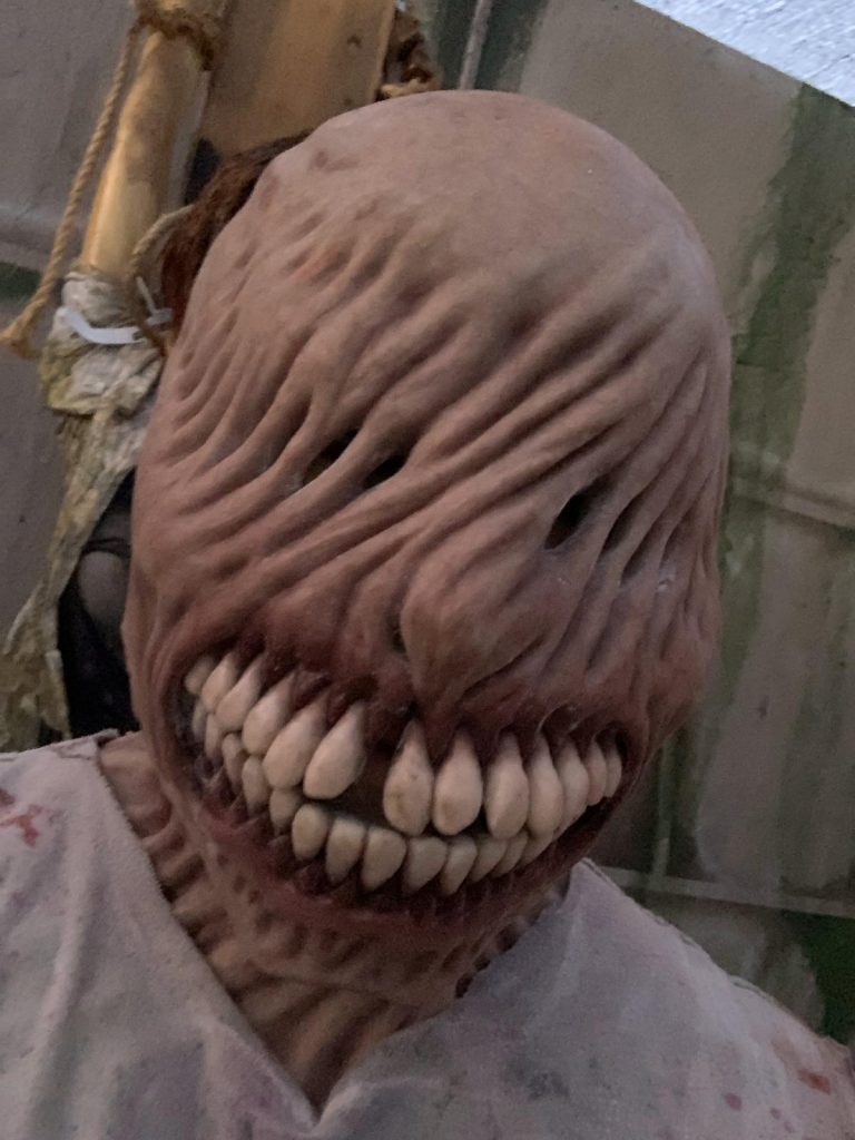 Scare actress in a special effects mask that twists the skin over the eyes and accents the gross yellow teeth