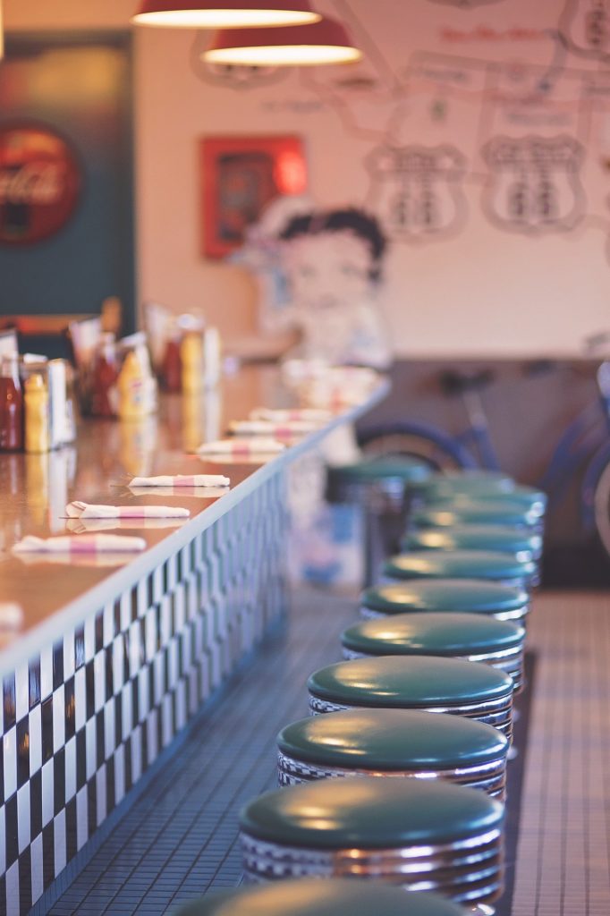 Counter of a 50's diner with swivel stools and a blurry Betty Boop in the back