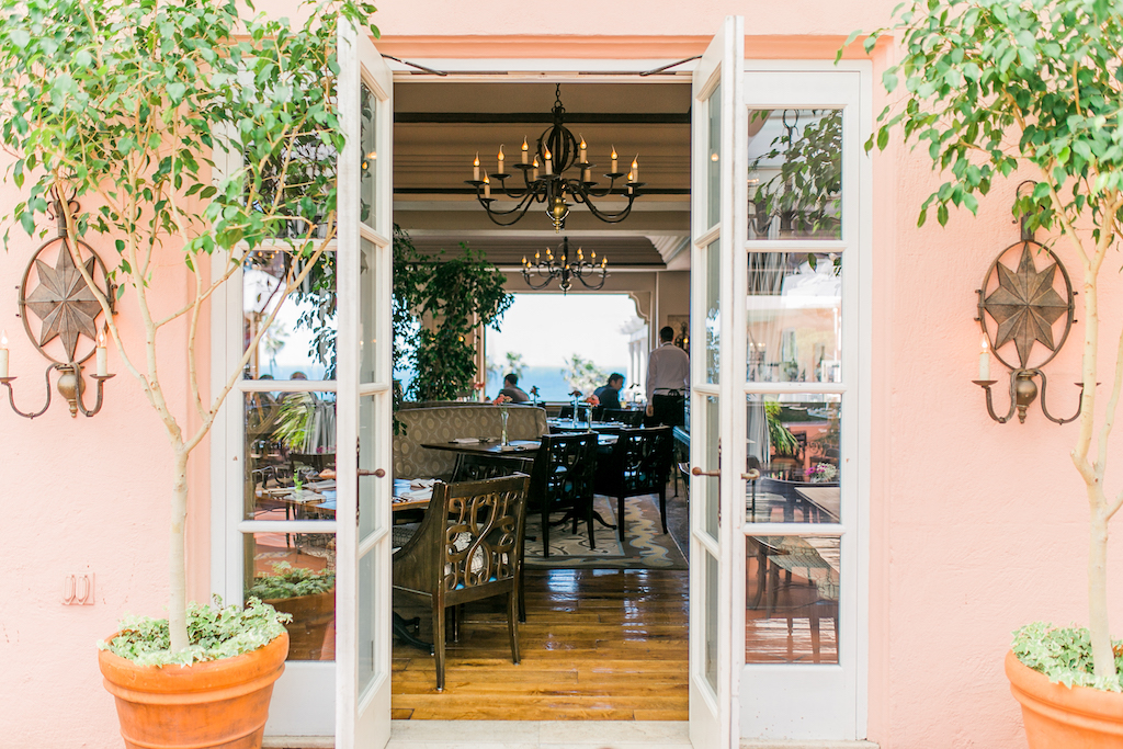 Pink walls break to a white glass door entrance to an elegant lit up dining room