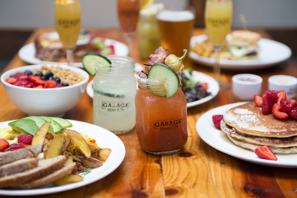 Plates filled with breakfast and lunch items clustered on a table with cocktails adorned with garnishes