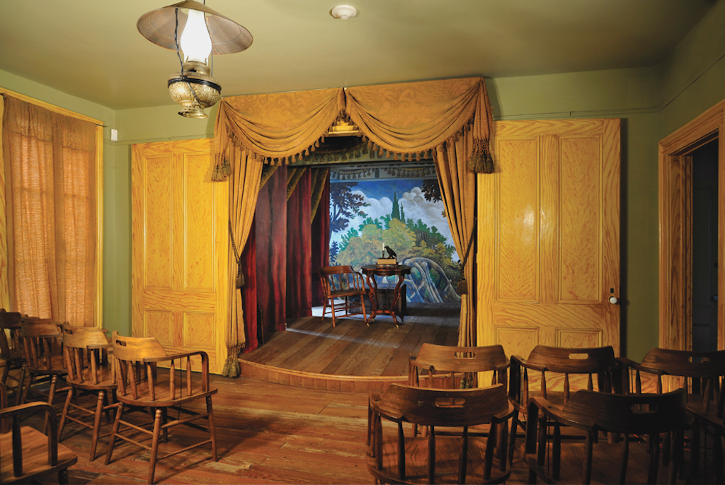 A small theater with dark wood seats, yellow wallpaper and curtains, and bright lighting