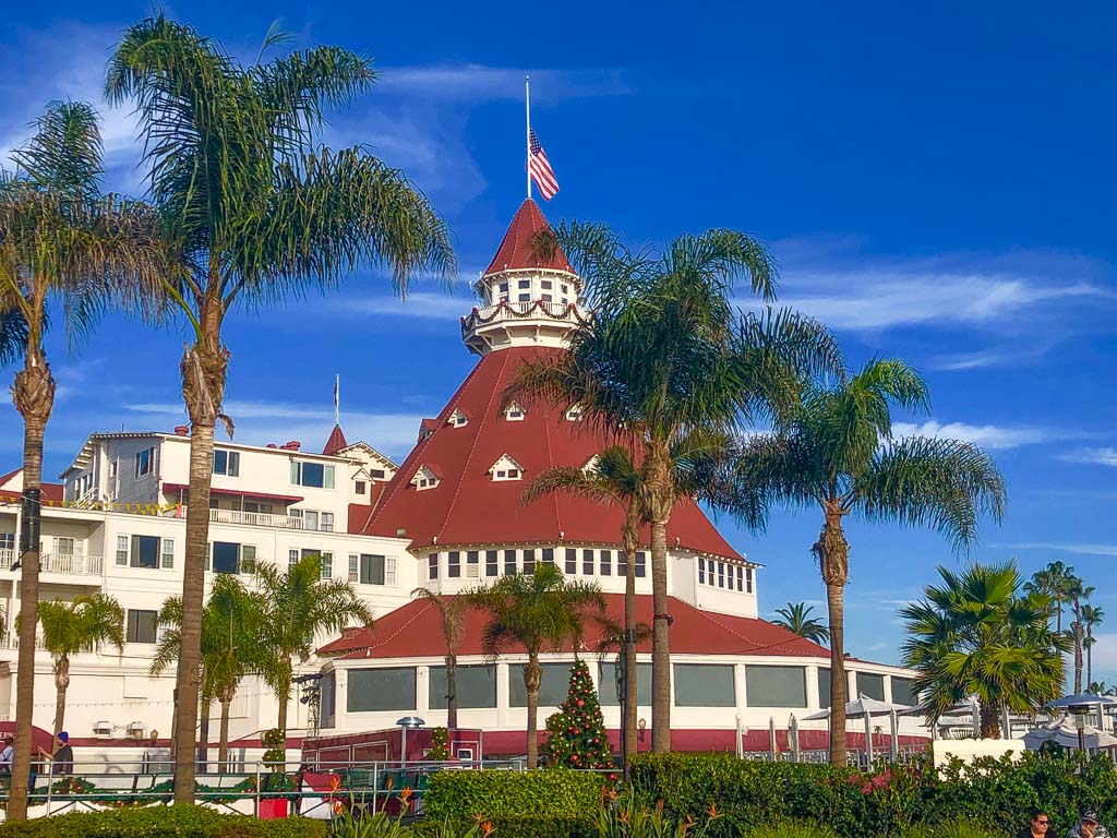 conical building with red roof and american flag on top with palm trees in the foreground and christmas decoration - Hotel Del Coronado