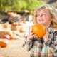 Little blond by holding pumpkin in the front with pumpkin patch in the background