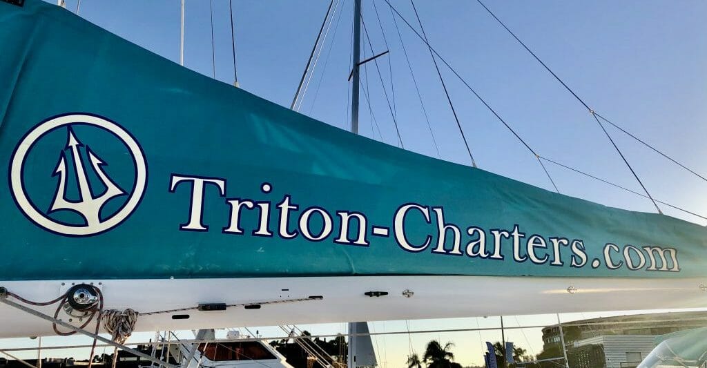 Teal sail with white writing: Triton Charter - San Diego Catamaran Cruise