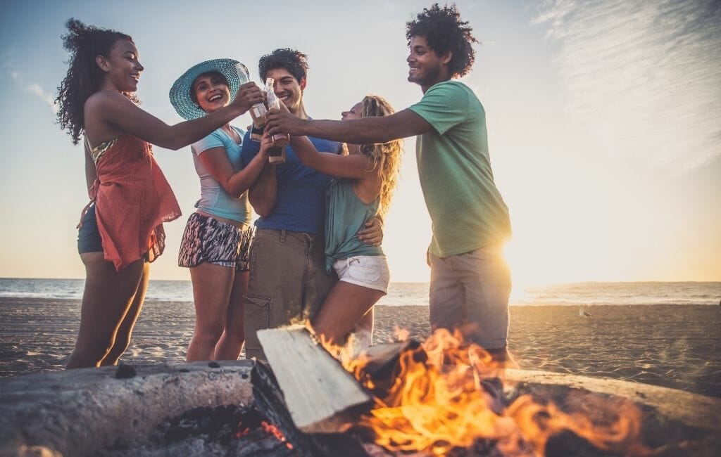 5 people toasting cheers at a beach bon fire in San Diego