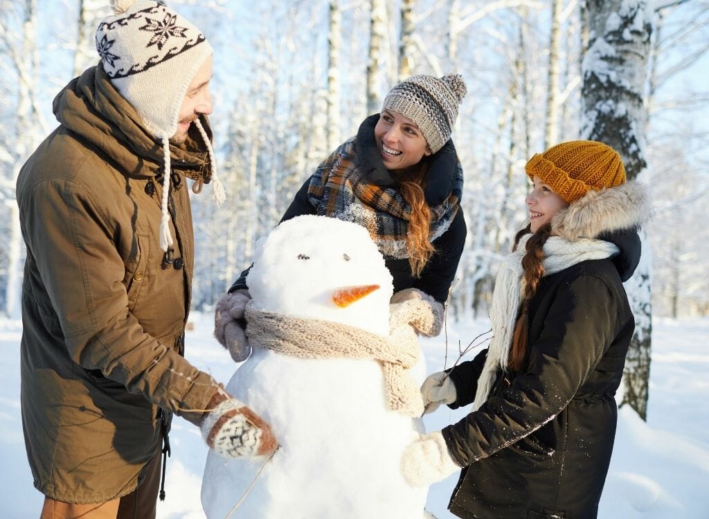 Family with one kid building a snow man in a wintery landscape