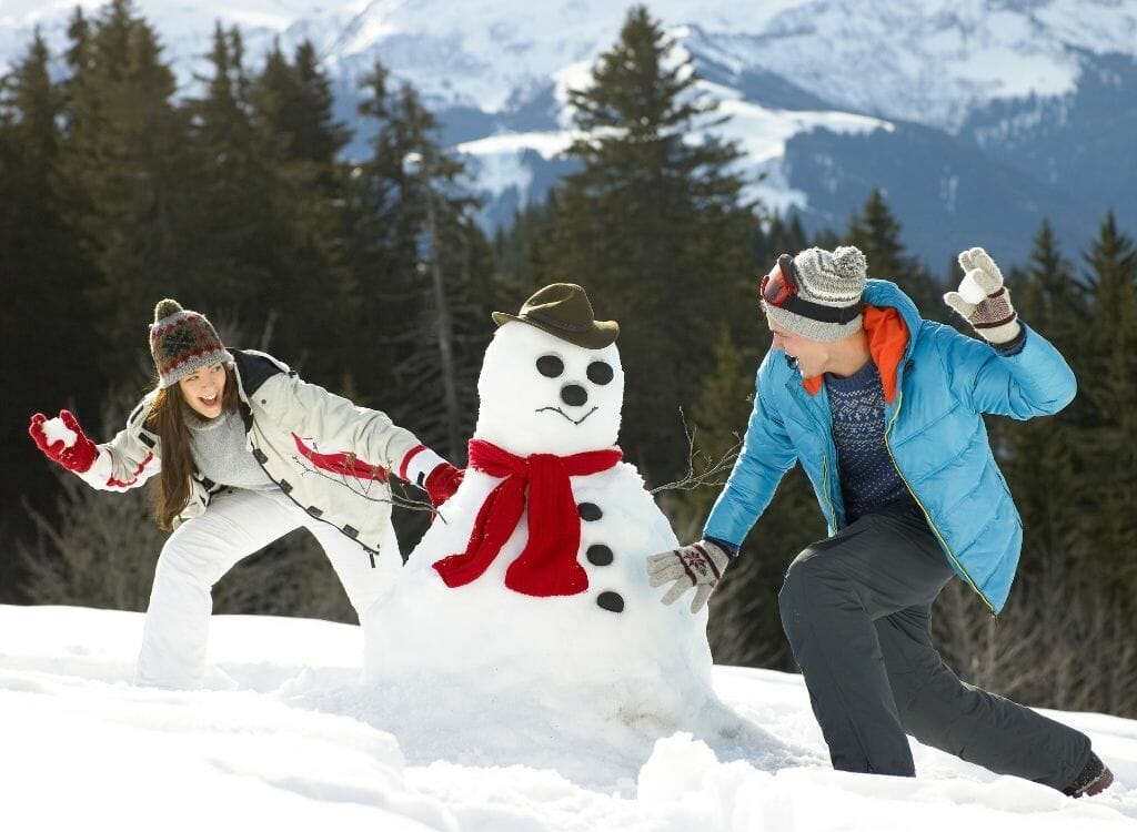 Couple having a snowball fight around a snow man
