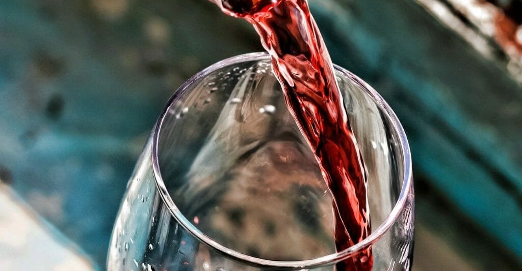 closeup of a wine glass and bottle top pouring red wine into glass -