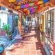 store fronts with terracotta tile walkway, white walls, wood covered path and colorful paper garlands