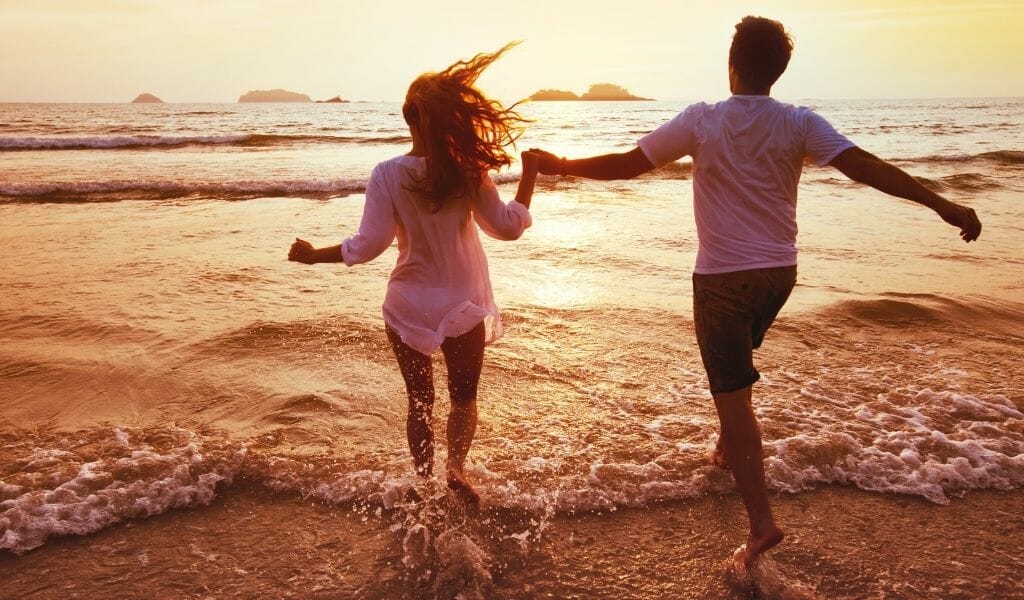 young couple running into the shallow water on the beach during sunset while holding hands