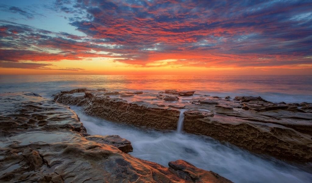 Long exposure sunset photo on Windandsea beach with water flowing over rock formation during colorful sunset