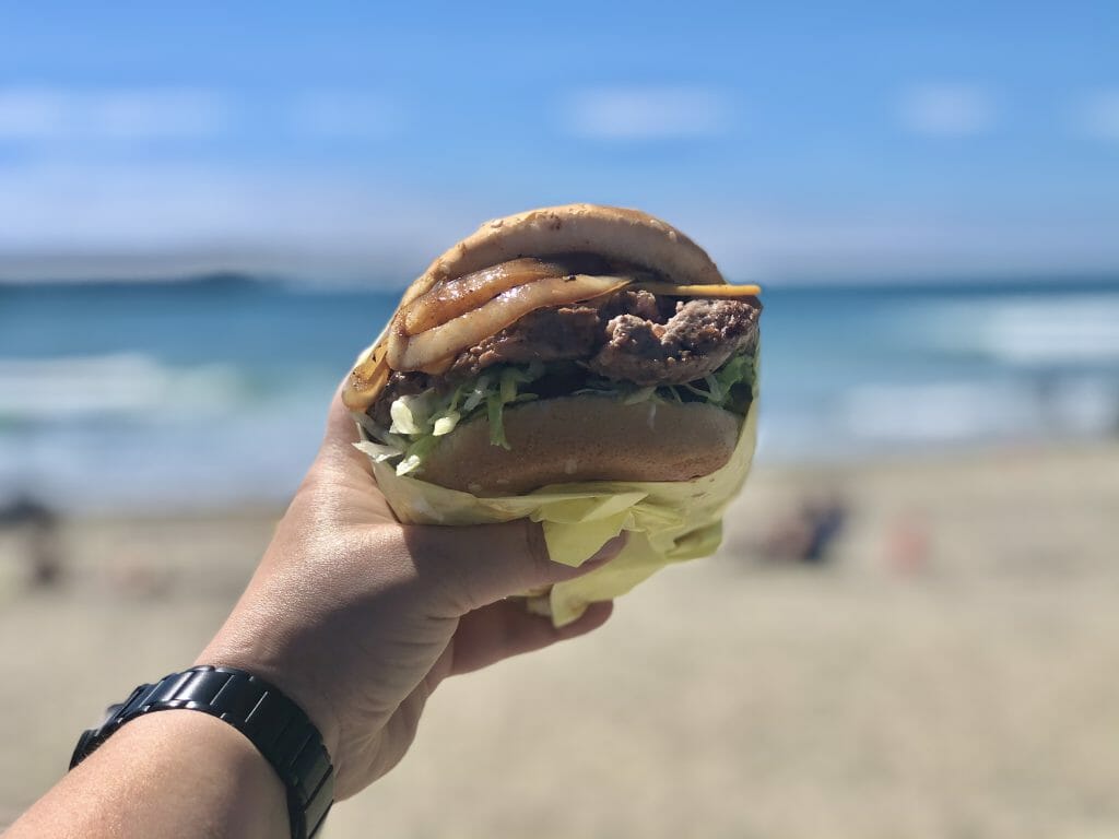 hand holding burger from Hodad's san Diego in front of the beach in Ocean Beach