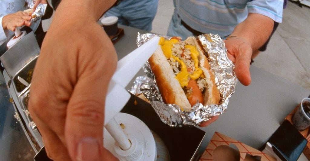Closeup of a man's hand pumping mustard on a hot dog at a baseball ballgame