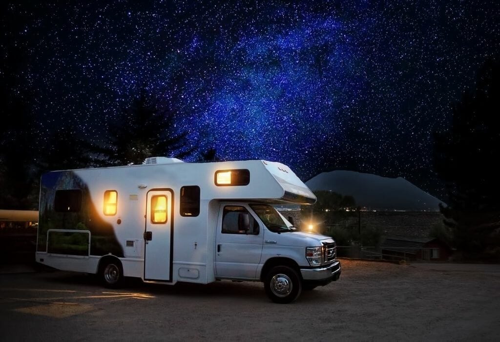 RV with lights on with a stary night sky in the background