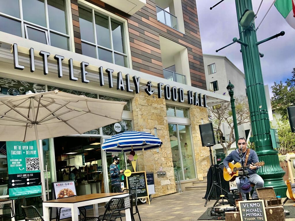 Man playing guitar and singing in front of Little Italy Food Hall San Diego - Live Music Piazza Della Famiglia Little italy