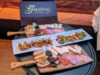 large black serving tray with two charcuterie boards and appetizer samplers with a brown menu with lettering: Greystone