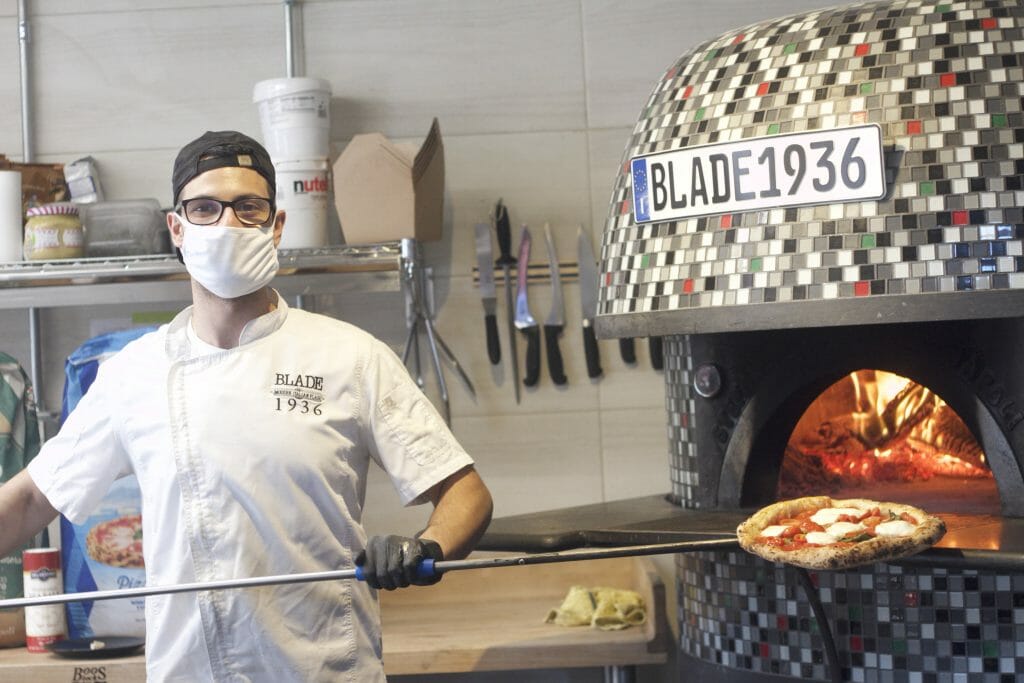 Man putting a pizza in a tiled pizza ovenBlade 1936 Antonio Zammataro Credit Aleya Zenieris