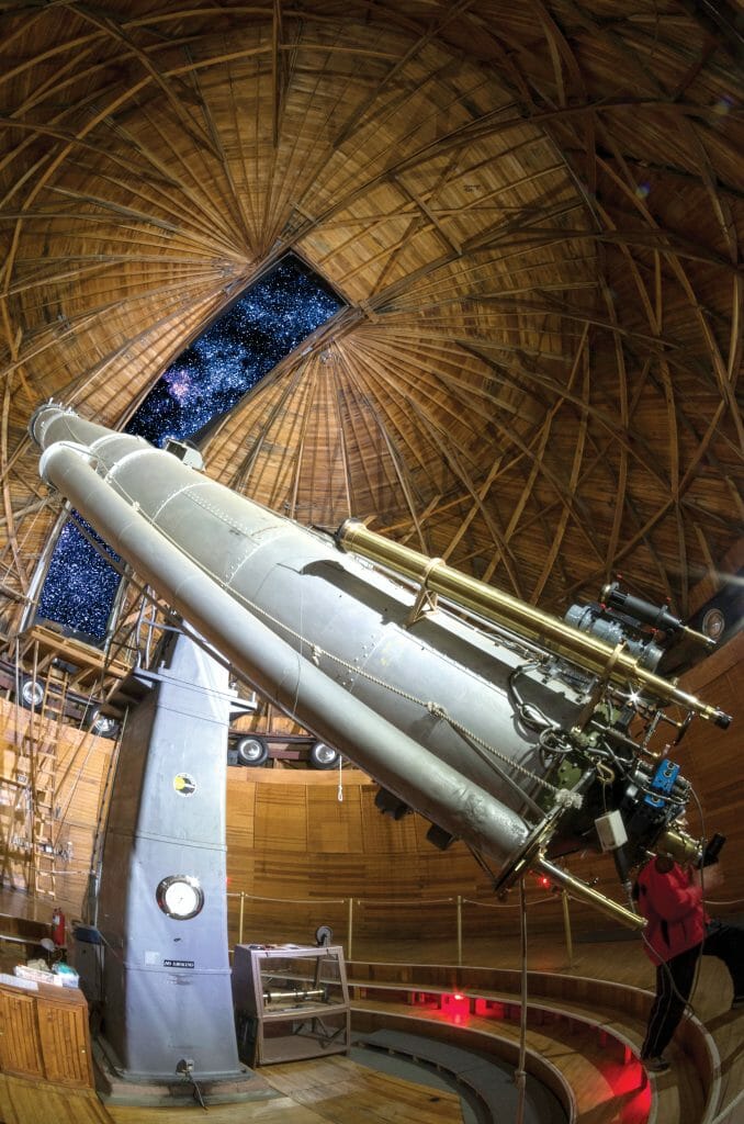 Large white telescope with wooden dome structure with opening showing the night sky