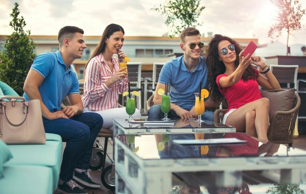 4 young people (2m/2f) drinking cocktails at a rooftop bar in San Diego