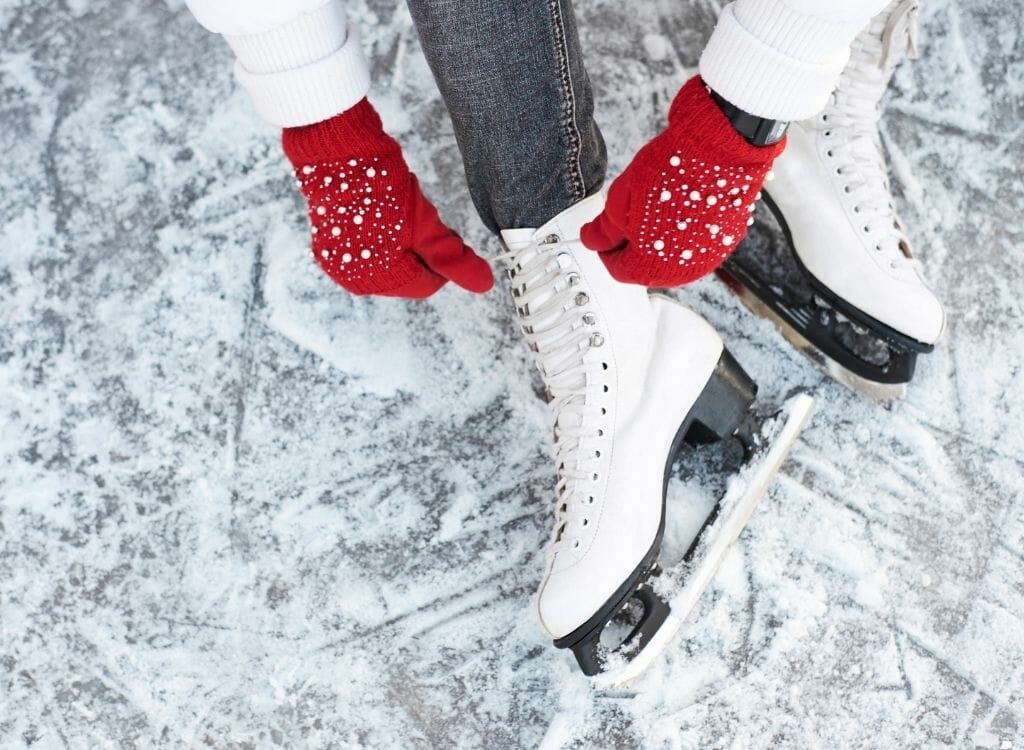 woman wearing red gloves tying her white leather ice skates