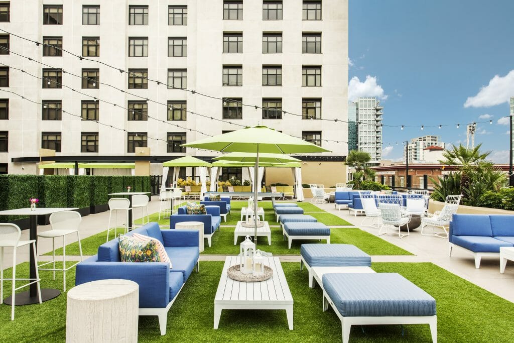 Rooftop bar at the Kimpton Solamar in San Diego with white outdoor couches with blue cushions on green fake grass and green umbrellas, background highrise and blue sky with clouds