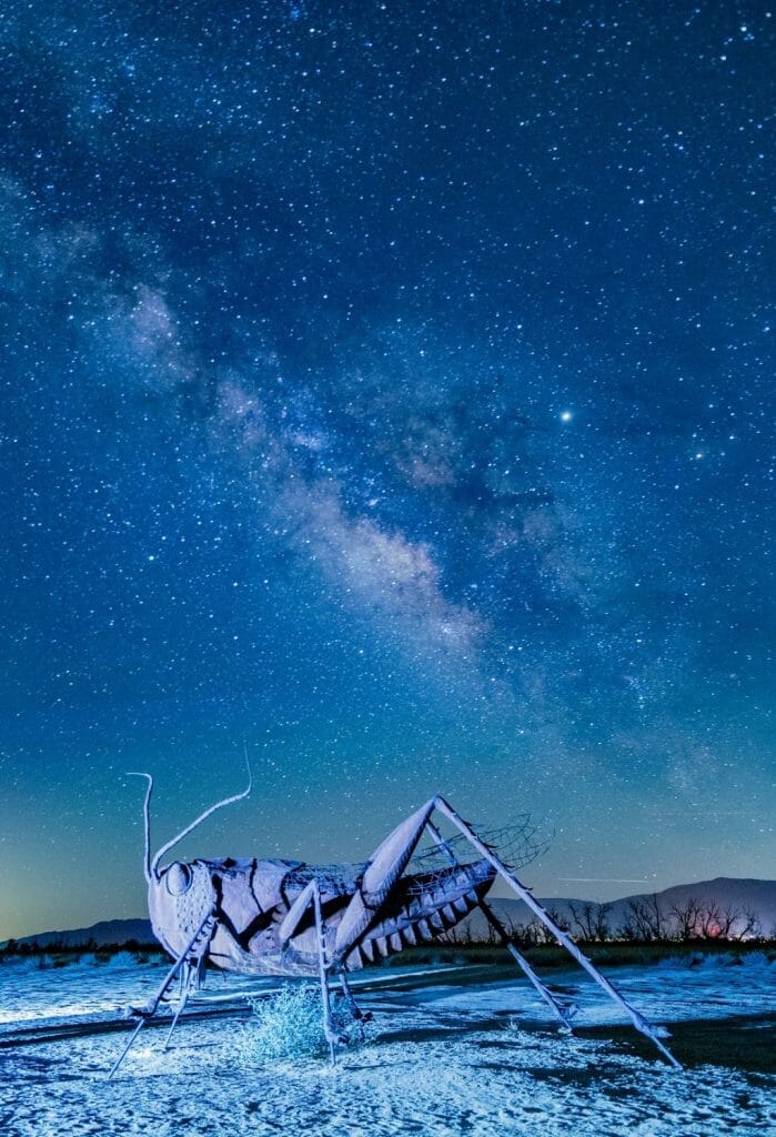 Oversized Metal Cricket sculpture in Anza Borrego at night with Milky Way and starry sky above - stargazing in San Diego