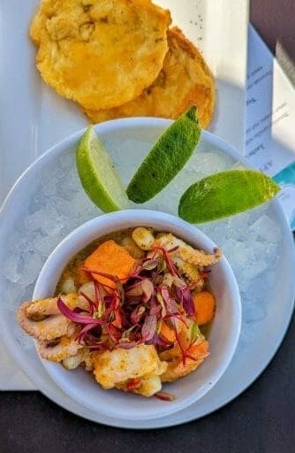 bowl with Ceviche on a bed of ice, sliced lime, and plantain fritters
