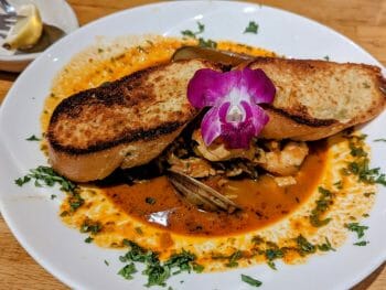 Chioppino seafood stew with garlic plate and decorated with a purple orchid