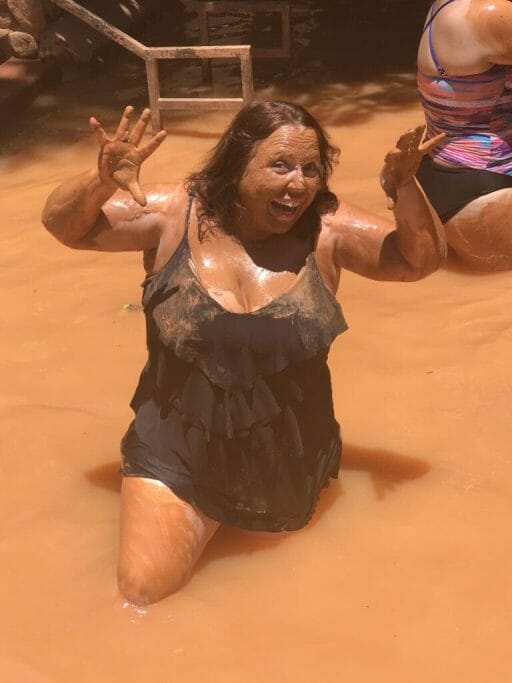 Woman in swimsuit standing in a pool of muddy water, covered in mud at Glen Ivy Club Mud
