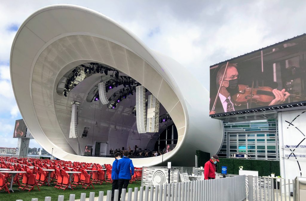 Close up of the Rady Shell Concert hall - a white shell outdoor concert venue with red chairs and large screens on the side of the stage