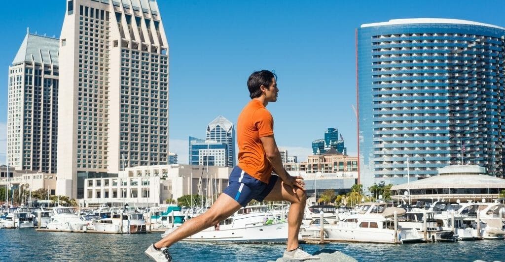 Male runner stretching on rocks in front of San Diego Skyline