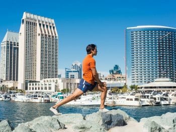 Male runner stretching on rocks in front of San Diego Skyline