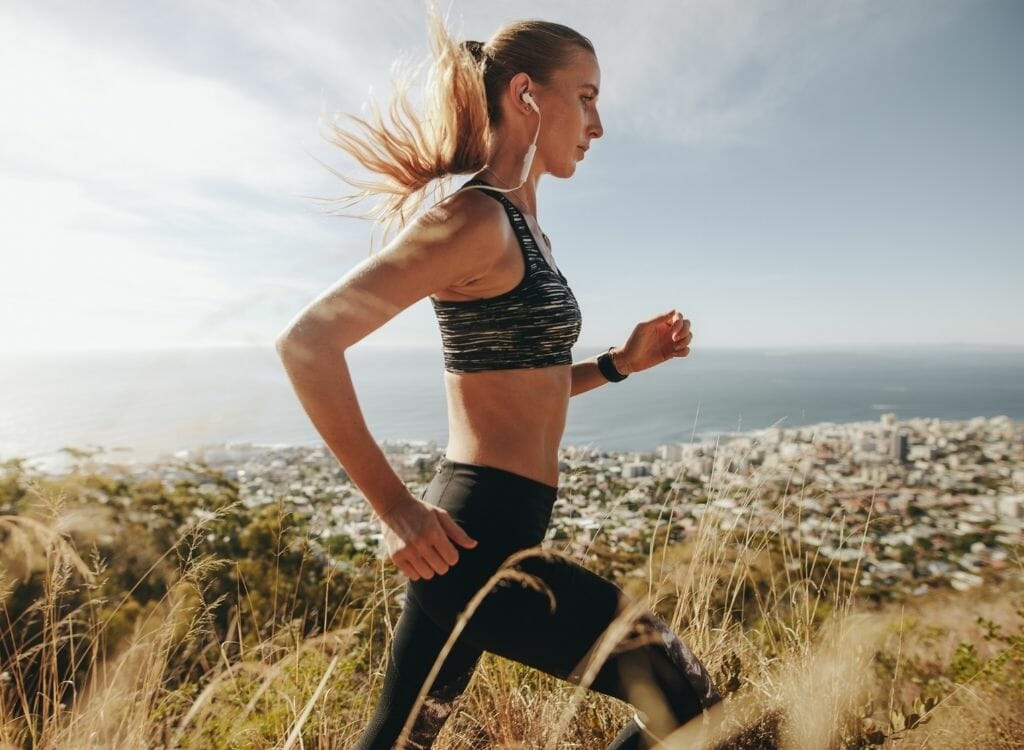 Female Marathon runner running on trail on a hill overlooking coastal beach town