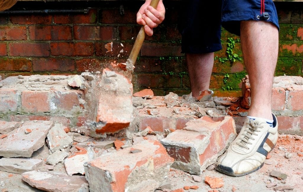 Closeup of a hand and feet of a man smashing brick with a sledgehammer