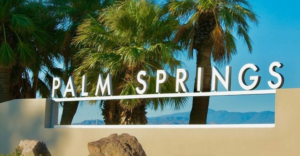 letter sign on top of tan colored wall spelling Palm Springs - Palm trees in the the background and blue sky
