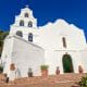 Mission San Diego Church - white Front with open bell tower with 5 bells, red brick walk way and dark blue sky
