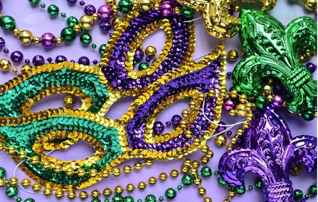 Table with two green and purple mardi gras eye masks and several green, purple, gold bead necklaces
