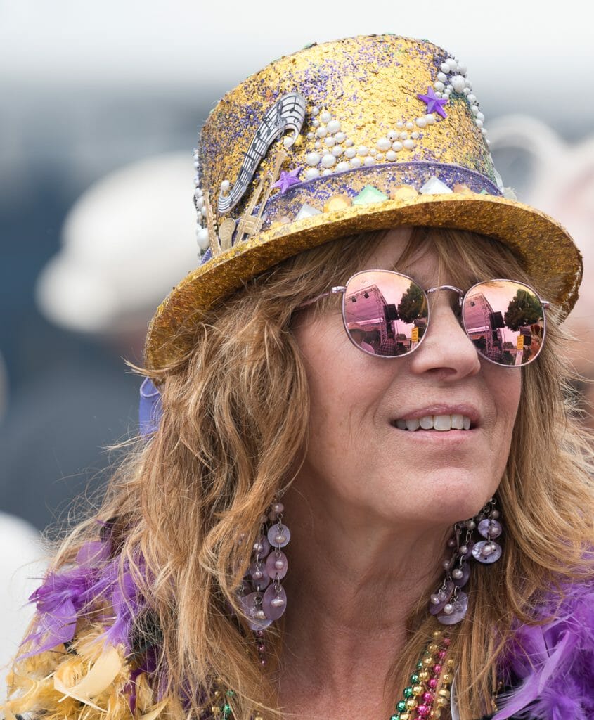closeup of a woman wearing golden glitter hat, purple fedora and pink sunglasses