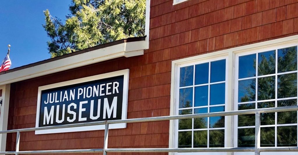 Red wood building with white trim and a black sign with white letters: Julian Pioneer Museum