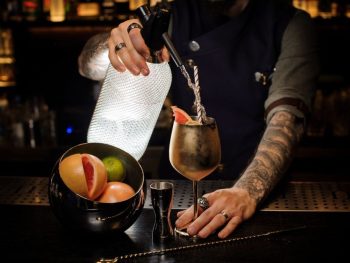 tattooed forarm mixing drinks at a bar - dark moody atmosphere like in a Speakeasy