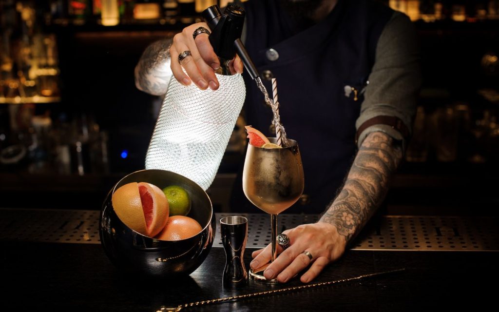 tattooed forarm mixing drinks at a bar - dark moody atmosphere like in a Speakeasy