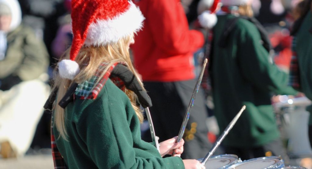 woman with santa hat and green jacket playing drums in Holliday Parade