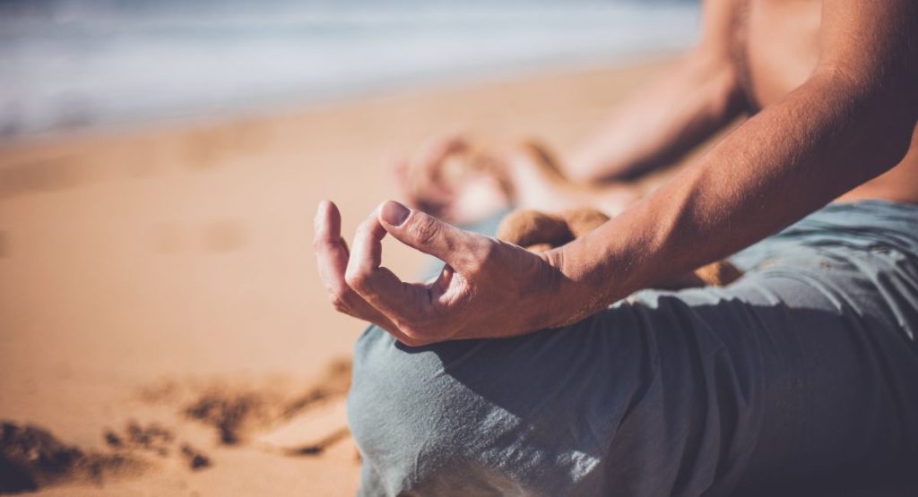 Closeup of man meditating on the beach, showing his hands and crossed legs