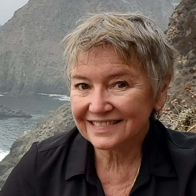 headshot of smiling woman with short hair in front of a rugged coast line
