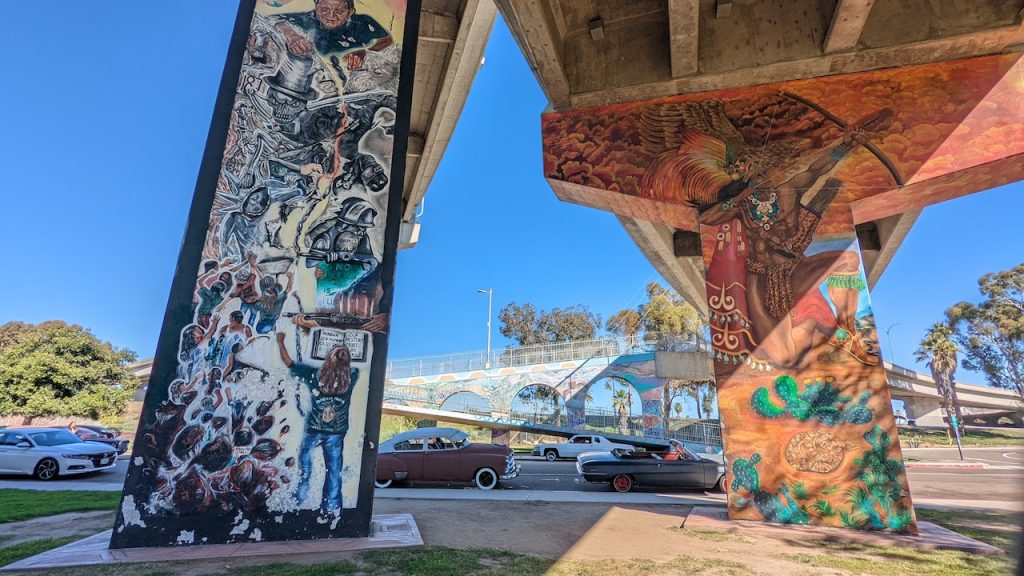 Large colorful murals painted on concrete Interstate support beams on sunny day. Chicano Park murals, Barrio Logan.